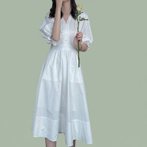 Person wearing a white dress holding a rose in front of a window with a view of greenery.